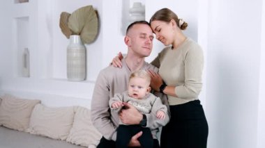 Sevgi dolu bir bebeği olan beyaz bir çift. Anne ve baba birbirlerine yaslanır, kadın kocasını nazikçe alnından öper..