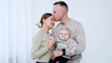 Bebek tutan bir adam karısını alnından öper. Mutlu beyaz bir ailenin portresi..