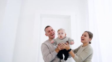 Gülümseyen beyaz bir çift kucağında küçük bir bebek taşıyor. Ebeveynler küçük oğullarına el sallıyor. Beyaz arkaplan.