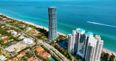 İnsansız hava aracı Atlantik Okyanusu kıyısındaki yüksek binalara yaklaşıyor. Otobanlarda bir sürü araba var. Sürat teknesi su yüzeyinden hızla geçiyor..