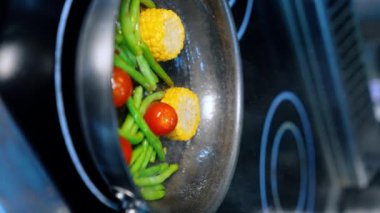 Fasulye ve mısır kızartma tavasında kızartılır. Siyah eldiveni ver, domates at ve sebzeleri karıştır. Kapatın. Dikey görünüm.