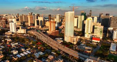 Güneşin batışının parlak ışığı Miami, Florida, ABD 'deki gökdelenleri aydınlatıyor. İnsansız hava aracı hareketli trafiği olan güzel şehrin üzerinde yükseliyor..