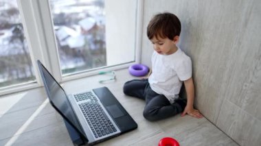 Balkonda dizüstü bilgisayarı olan sevimli beyaz çocuk. Tatlı çocuk klavyedeki tuşlara basıyor. Üst görünüm.