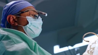 Maskeli ve hoparlör gözlüklü beyaz erkek cerrahın yüzü. Profesyonel işlemde düşük açı görünümü.