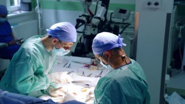 Beyaz erkek doktor, hoparlörlü gözlük takıyor ve ameliyat yapıyor. Doktora yardım etmek cerraha yardımcı olur..