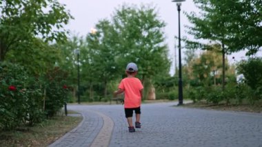 Güzel küçük erkek çocuk yeşil parkın yanından geçiyor. Çocuk şapkasını çıkardı ve tekrar giydi ve gitti..