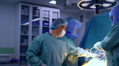 Ameliyat için hazırlanan hastanın yanında üç cerrah duruyor. Doktorlar cihazları ameliyatta kullanılacak şekilde ayarlıyorlar..