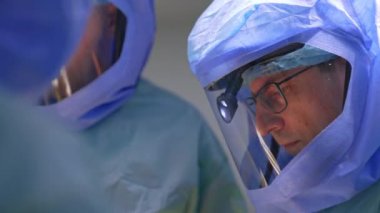 Koruyucu kask takan doktorlar operasyonda birlikte çalışırlar. Gözlüklü cerrah tahta tokmak kullanır..