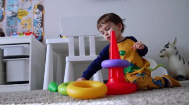 İki yaşında bir çocuk yerde oturuyordu. Küçük çocuk piramidi birleştirir ve ayağa kalkar..