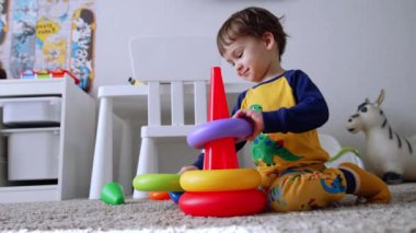 Tatlı erkek bebek oyuncak piramidinin yanında yere oturuyor. Çocuk oyuncağı neşeyle monte ediyor. Düşük açı görünümü.