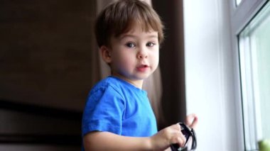 Sevimli, tatlı erkek bebek pencerede duruyor. Güneş gözlüğü tutan sevimli çocuk dışarıya bakıyor..