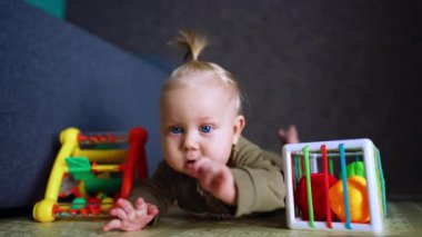Israrcı küçük oğlan kameraya doğru sürünüyor. Kapatın. Bebek oyuncakların etrafında hareket ediyor..