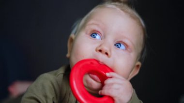 Mavi gözlü, sarı saçlı, sevimli, beyaz bir bebek. Güzel çocuk kırmızı plastik yüzük çiğniyor. Kapat..