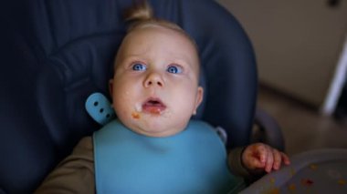 Yüzünde yemek olan sürpriz bir bebek yukarı bakıyor. Annem kaşığı bir çocuğun ağzına yemek ile sokuyor. Kapat..