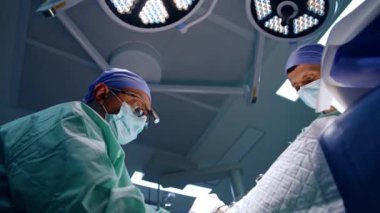 Deneyimli bir doktor ameliyat masasında oturuyor. Ameliyathanede çalışan sağlık görevlilerinin görüş açısı düşük..