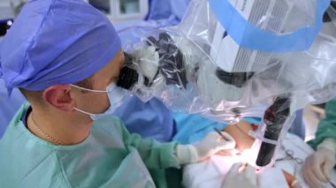 Sakin, kendinden emin cerrah metal aletlerle mikroskop başında oturur. Doktorun elinde ameliyat yaparken yüksek açılı görüntüsü var..