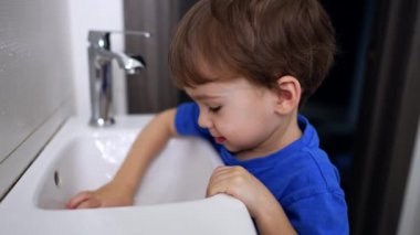 Sevimli beyaz çocuk lavabonun yanındaki banyoda duruyor. Kanalizasyonla oynayan sevimli bir çocuk. Kapat..