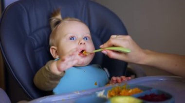 Sarışın bir bebeği kaşıkla beslemek. Annem sevgili oğluna portakal püresi veriyor..