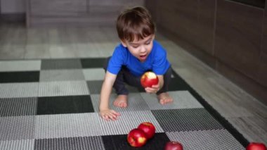 Sevimli çocuk yere çömelmiş halının üzerinde birkaç elmanın yanında. Çocuk bir meyve koparır, bir ısırık alır, yerine koyar ve ayağa kalkar..