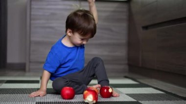 Mutfakta yerde oturmuş gülümseyen siyah saçlı bir bebek. Güzel çocuk kırmızı elmalarla oynuyor..