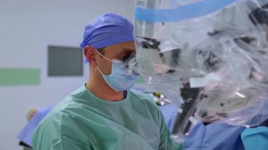 Kendine güvenen bir cerrah mikroskoba dikkatlice bakar. Mikro cerrahi yapan bir beyin cerrahının portresi.