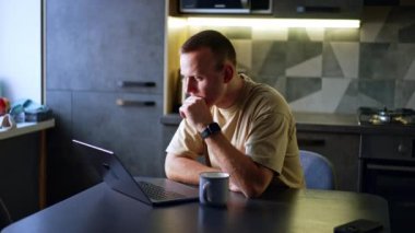 Düşünceli adam dizüstü bilgisayar ekranına bakarak oturur. Evden çalışan bir adamın portresi.