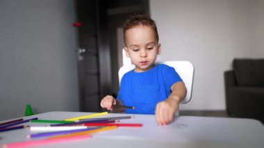 Sakin küçük çocuk çizim yapmakla meşgul bir şekilde masada oturuyor. Yeni yürümeye başlayan çocuk elinde kahverengi bir kalemle kağıdı daha da yakına çekiyor..