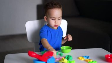 Sevimli küçük çocuk masada oturup plastikle oynuyor. Sevimli çocuk evde huzur içinde oynuyor. Bulanık arkaplan.