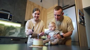 Şirin tombul bebek pastanın önündeki masaya oturur. Annem pastadaki mumu yakıyor. Aile evde kutlama yapıyor. Düşük açı görünümü.
