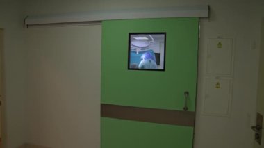 Açık yeşil sürgülü kapıya yaklaşıyoruz, penceresi olan kapıya. Büyük tıbbi ekip odanın içinde operasyon düzenliyor..