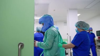 Kadın hemşire bornozu cerraha bağlıyor. Modern hastanede operasyonel prosedüre hazırlanan tıbbi personel.