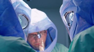 Koruyucu miğferli üç sağlık görevlisi. Doktor ameliyathanede işbirliği yapıyor..