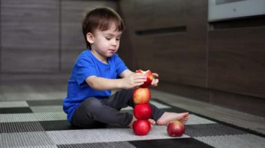 Sevimli beyaz çocuk kırmızı elmalardan bir kule inşa ediyor. Çocuk yere oturup elmaların düşüşünü ve yuvarlanmasını izliyor..