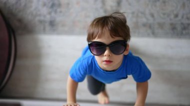 Annesinin güneş gözlüğünü takan beyaz, tatlı bir çocuk. Sevimli bir çocuk hava öpücüğü yolluyor ve uzaklaşıyor. Üst görünüm.