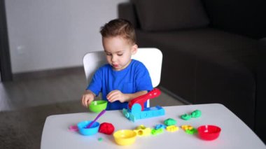 Masada oturan tatlı çocuk plastikle oynuyor. Yeni yürümeye başlayan çocuk bir parça plasticin ve onu kesmek için bir sopa alır..
