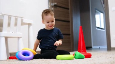 Evde piramit inşa eden güzel, gülümseyen bir bebek. Yerde oturan sevimli çocuk oyuncakla oynuyor..