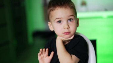 Siyah tişörtlü siyah saçlı beyaz çocuk sandalyede oturuyordu. Annenin eli bebeğine tam bir kaşık veriyor. Bulanık arkaplan.