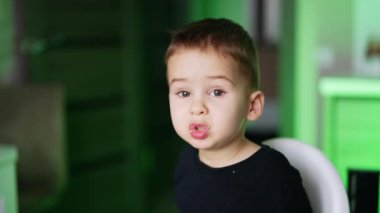 Şirin küçük çocuk oturup yemek yiyor. Çocuk yemek sırasında konuşuyor. Kapatın. Bulanık arkaplan.