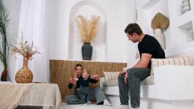 Annem kucağında küçük bir bebekle yerde oturuyor. Sevimli çocuk babasının kanepesinde oturuyor..