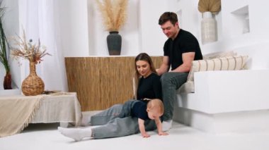 Kadın, kocasının yanında, kanepede oturuyor. Aileler, yerde sürünen küçük şirin bebeklerini seyrederler..