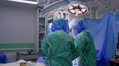 Cüppeli ve kasklı cerrahlar yuvarlak lambalar altında bir hastayı ameliyat ediyorlar. Modern kliniklerde travma cerrahisi süreci.