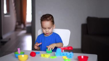 Güzel küçük çocuk masanın yanındaki plastikçeyi yuvarlıyor. Yaratıcılık, sanat ve oyun konsepti.