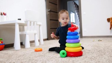 Güzel beyaz çocuk oyuncak piramidinin arkasında oturuyor. Evde oynayan küçük bir çocuk yerde oturuyor..