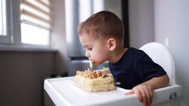 Sevimli bebek önünde duran pastaya eğiliyor. Çocuk pastayı ısırır ve mutlu bir şekilde alkışlar..