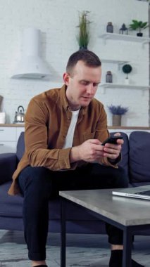 Dairesinde çalışan genç bir serbest çalışan. Evde dizüstü bilgisayarın önünde cep telefonu kullanan bir adam. Yakışıklı adam, serbest işinde aletler kullanıyormuş. Dikey video