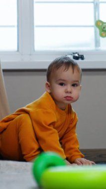 Sakin küçük bebek hareketsiz oturuyor ve dikkatlice kameraya bakıyor. Sevimli çocuk gülümsedi ve emeklemeye başladı. Dikey video