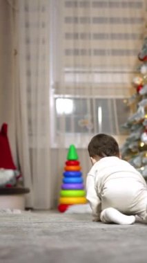 Yürüyen çocuğu takip ederek hızla yerde sürünüyorlar. Ağzında emzik olan bebek merdivenleri tırmanmayı hedefliyor. Noel ağacı arka planda. Dikey video