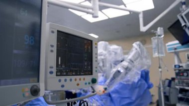 Ameliyat sırasında çalışan akciğer ventilatörü monitörleri. Arka planda plastik kaplı Da Vinci robotu.