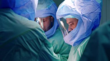 Travma cerrahisinde çalışan erkek cerrahi ekibi. Koruyucu miğferli beyaz doktorlar prosedürde işbirliği yapıyorlar..