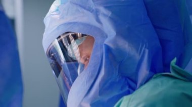 Kasklı bir erkek doktorun sakin yüz ifadesi. Cerrahi uzmanı operasyon üzerinde çalışıyor. Yan görünüm kapat.